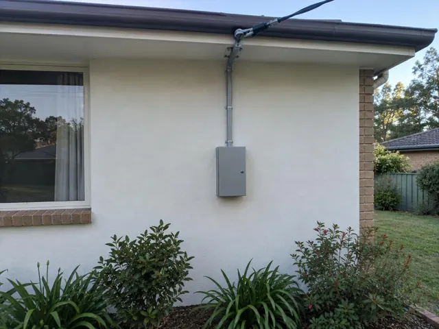 External house wall with overhead service cable and point-of-attachment bracket above a meter box in Glenning Valley